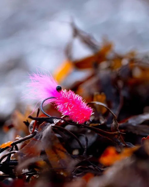 En starkt rosa fiskedrag med fjädrande svans ligger på torkat sjögräs, redo för passionerade fiskeentusiaster.