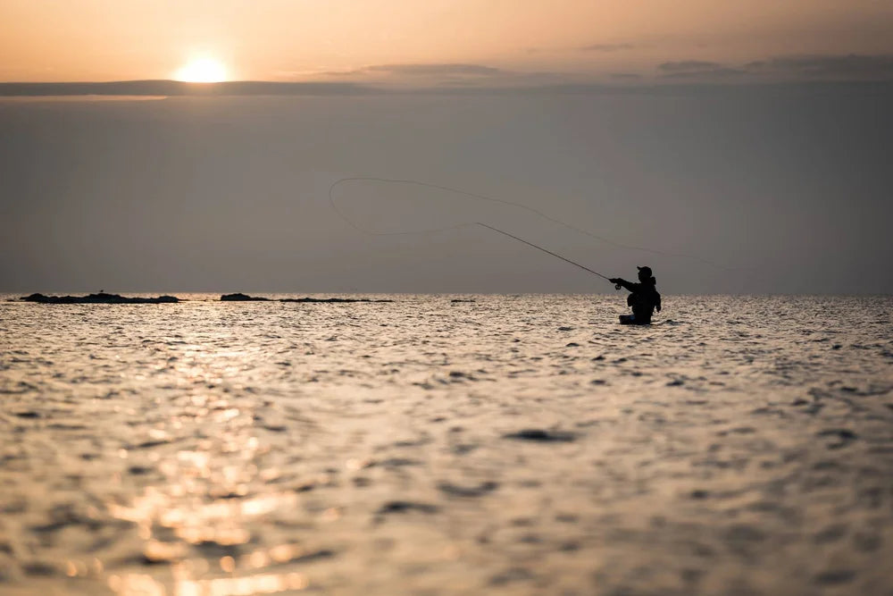 Silhuett av sportfiskare som kastar ut i havet vid solnedgång, fångar känslan av fiskeäventyr och resor.