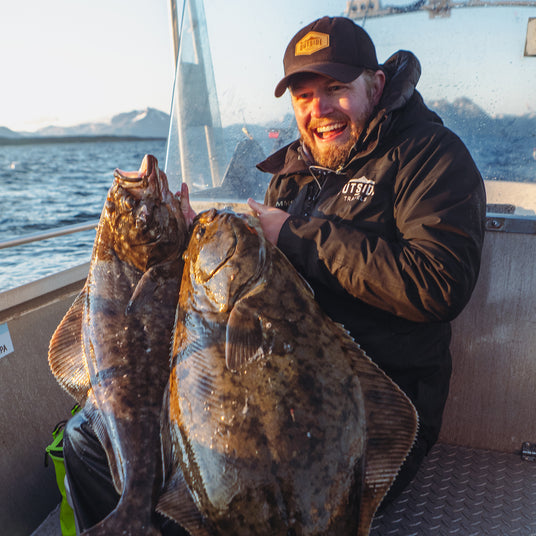 Glad sportfiskare i båt håller två stora fiskar, med fjord och berg bakom sig under Fiskeresa Frovåg Havsfiske Norge.