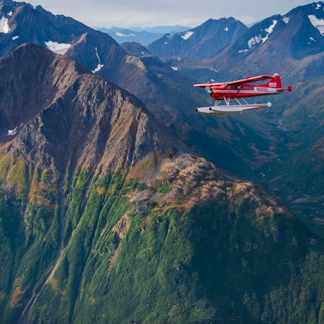 Rött sjöflygplan över snötäckta berg i Alaska på väg ut till fiskelodgen