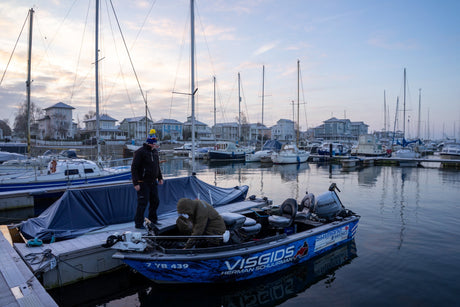 Två sportfiskare står på en liten blå fiskebåt vid bryggan bland segelbåtar i Nederländerna