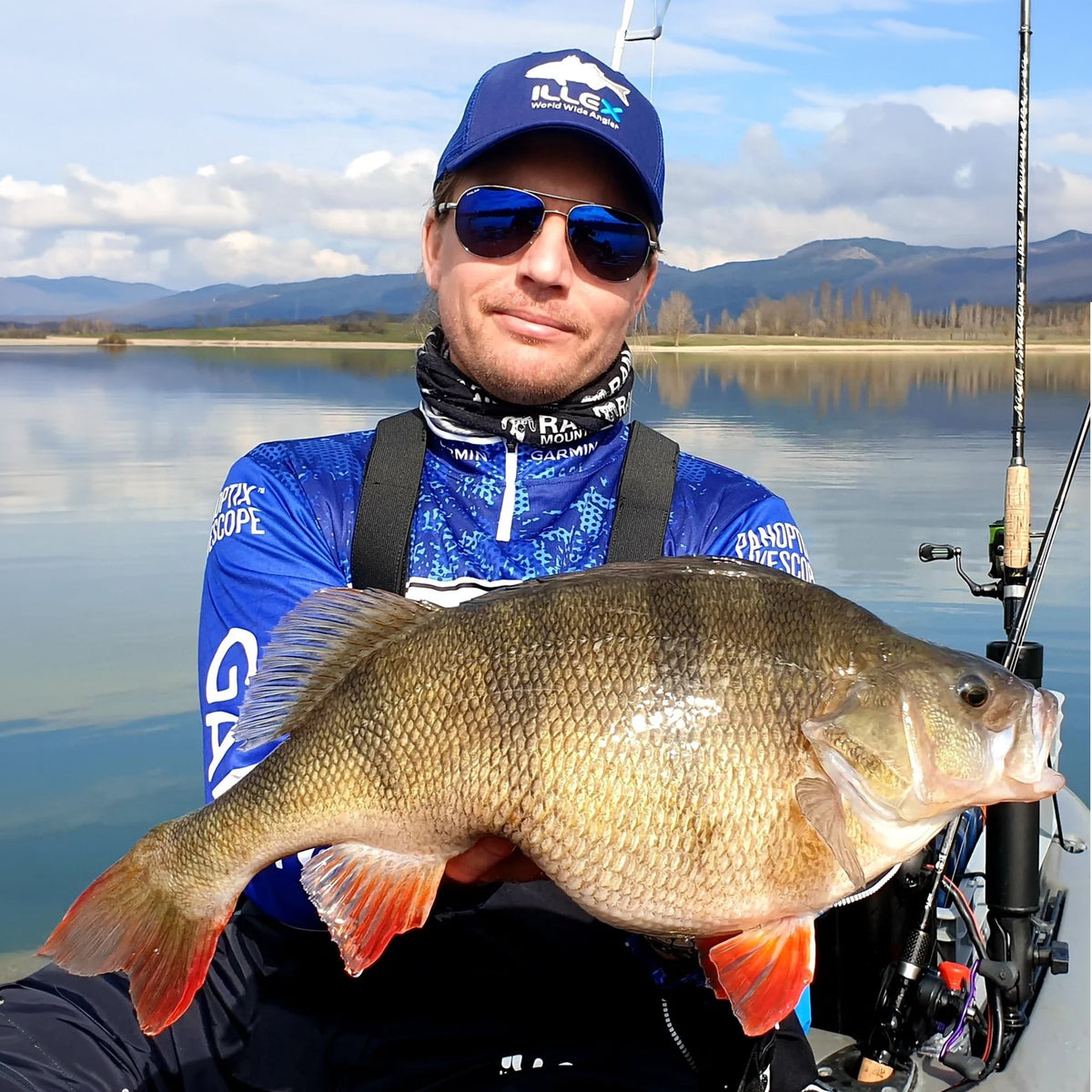 Sportfiskare i blå fisketröja håller en stor abborre vid sjön i Perchzilla