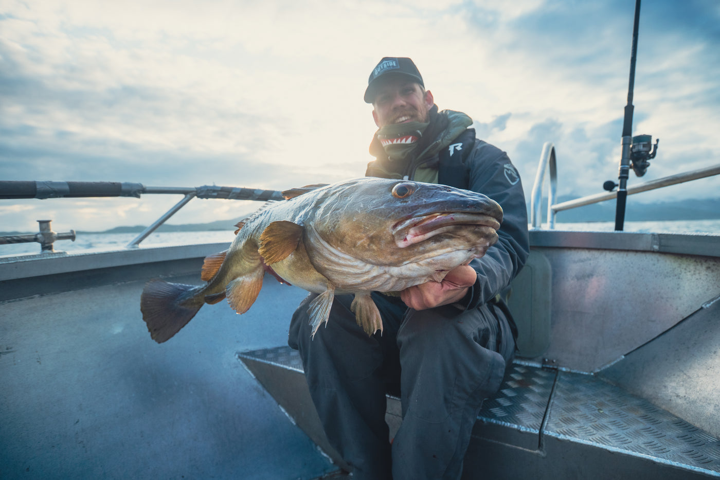 Sportfiskare i båt visar stolt upp sin fångst mot kameran, med solen och fiskeutrustning synliga i bakgrunden.
