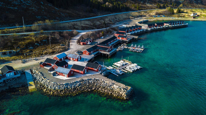 Flygbild över rorbuer och hamn vid turkost vatten i Lofoten