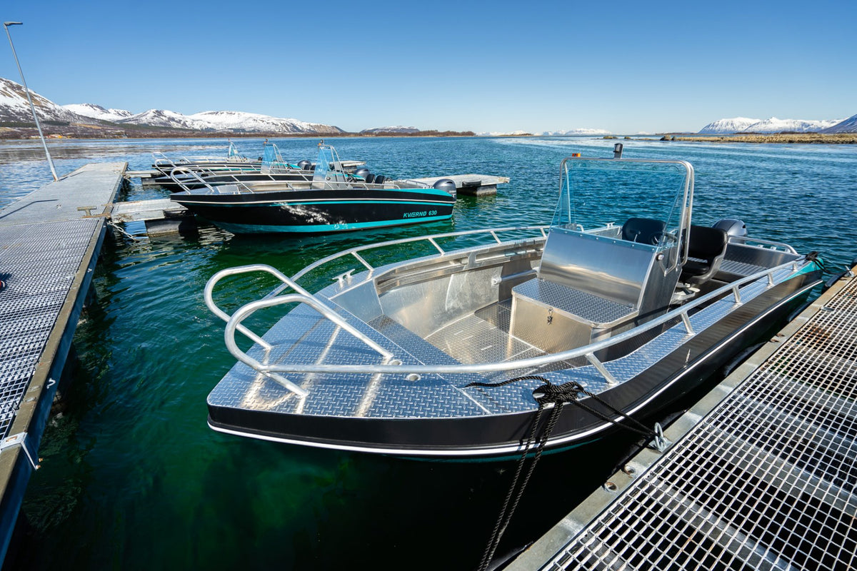 Aluminiumbåtar med turkosa detaljer vid brygga, solig dag och snötäckt fjäll - idealiskt för fiskeresa och sportfiske.