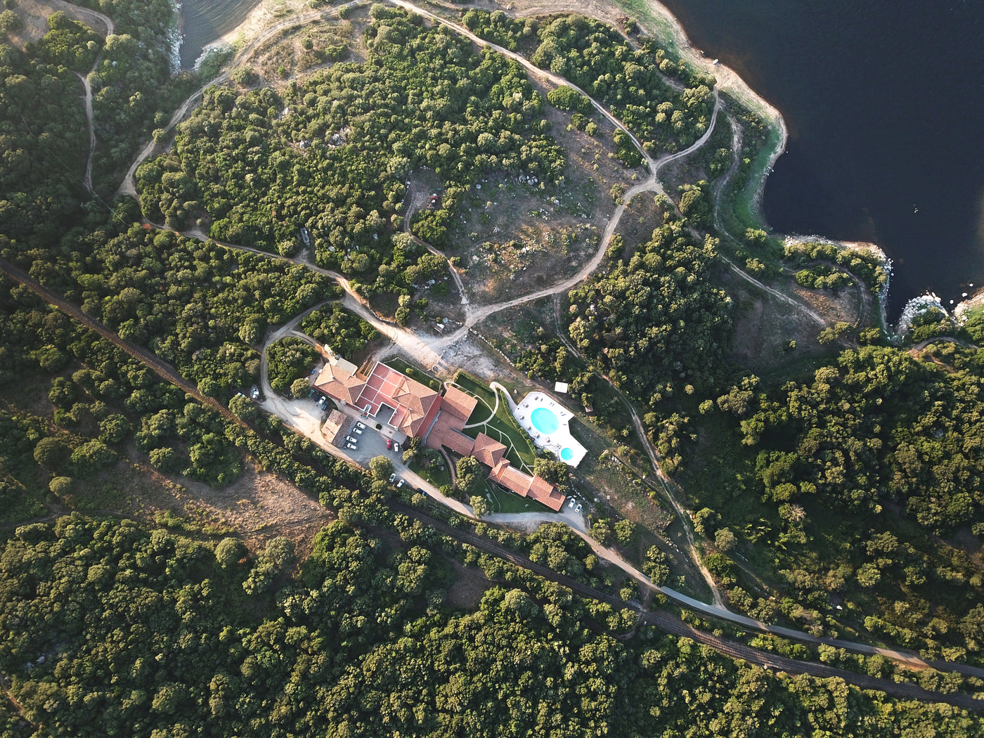 Flygfoto över stort hus med pool, omgivet av grönska och slingrande stigar, idealiskt för sportfiskare nära fiskevatten.