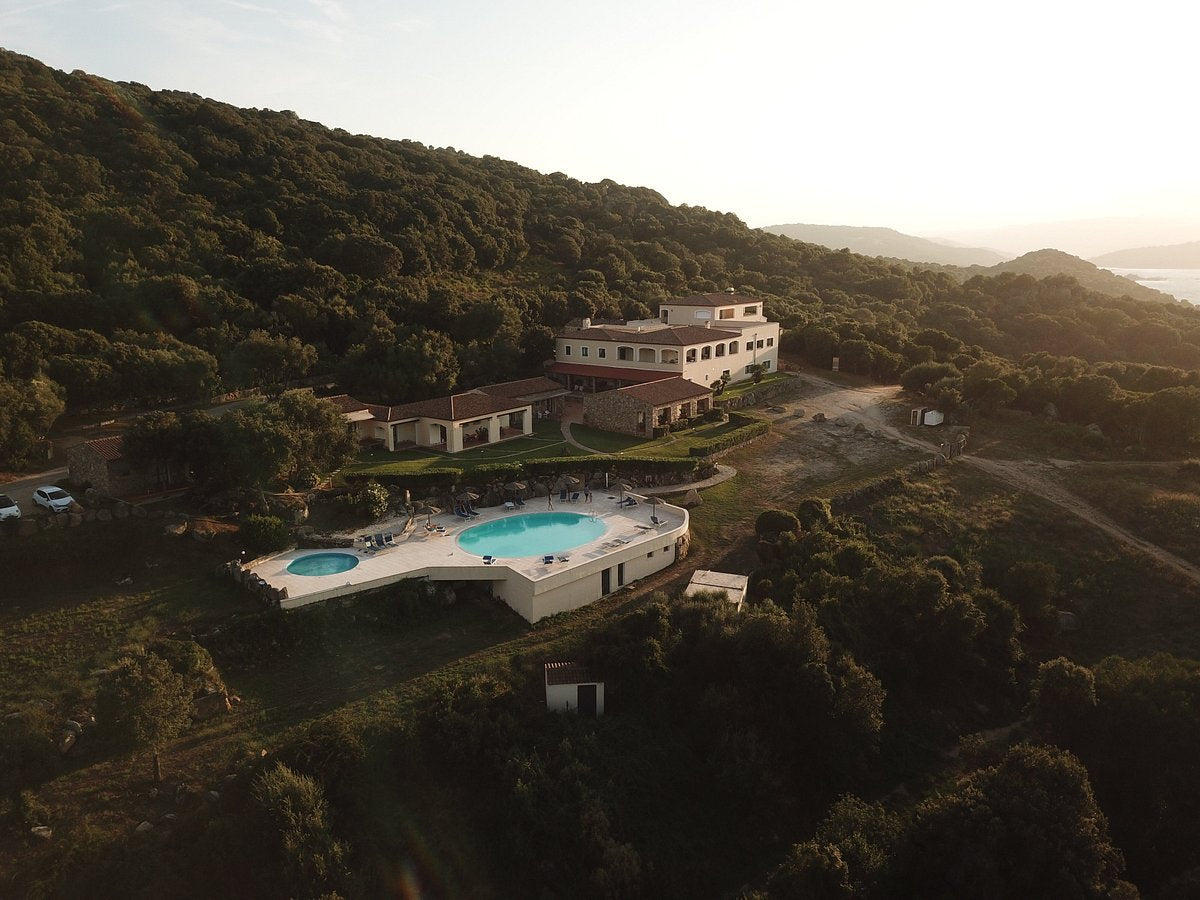 Flygfoto av stor villa bland gröna kullar med pool, solsängar och mindre pool-perfekt fiskesemester i solnedgången.